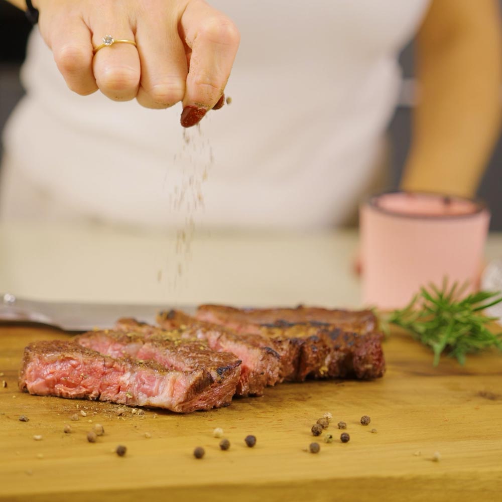 Gemahlener Pfeffer wird auf ein frisch gebratenes Steak gestreut.